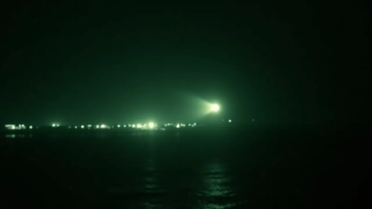 Grainy green and black infrared FLIR thermal footage of a small glowing object skimming low over a dark coastal airport at night and splitting in two