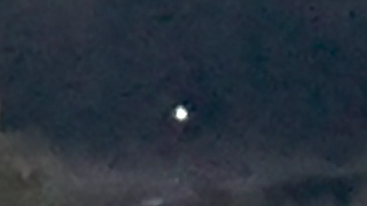 A bright white orb hovering against a darkening dusk sky above a treeline, from civilian cellphone footage released in PURSUE Release 03