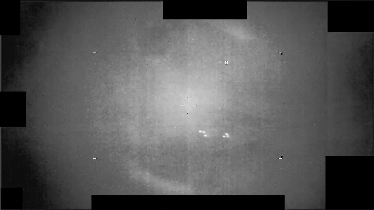 A grey infrared sensor display with a crosshair at center and a small cluster of bright points below it, filmed over open water in the Middle East in 2025