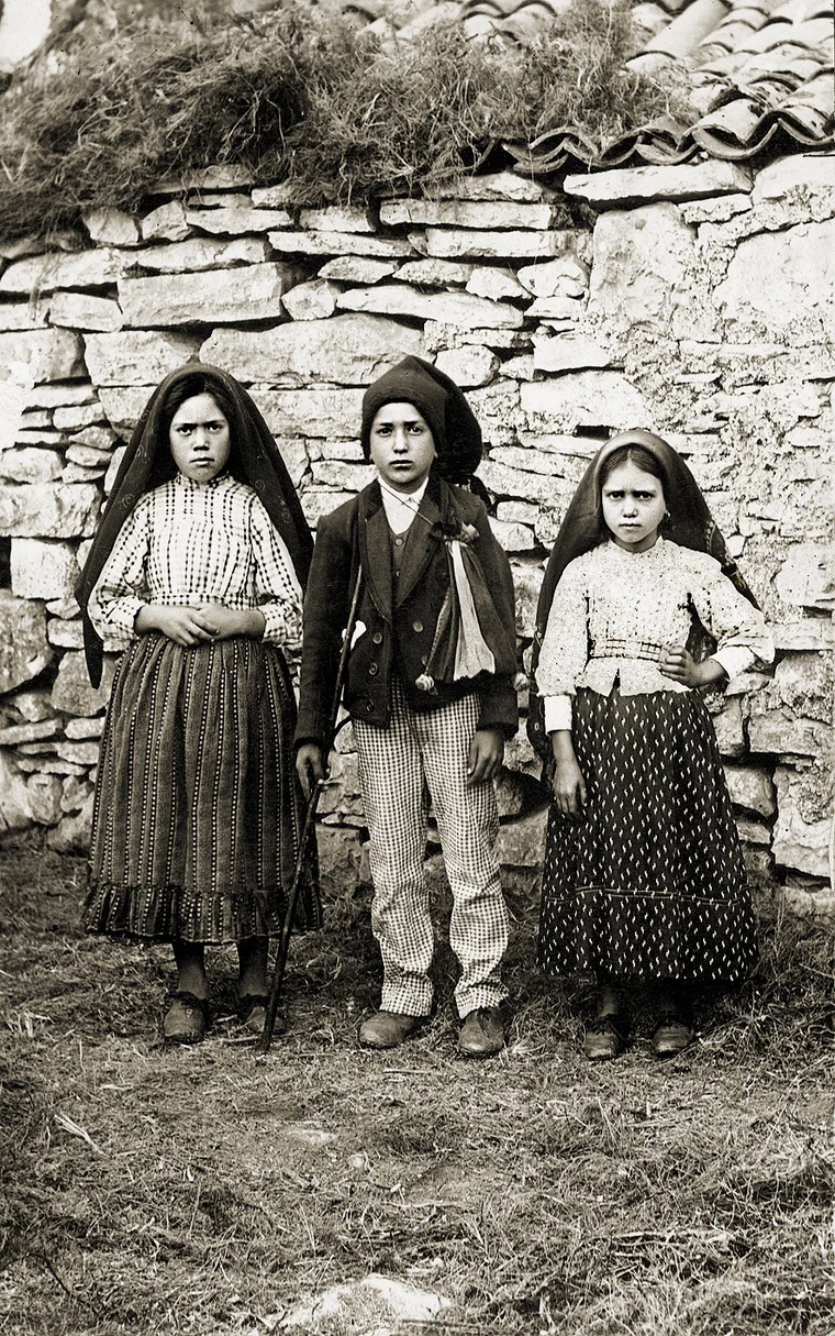 Studio portrait of the three shepherd children of Fatima in 1917, two girls in headscarves and a boy in a cap and jacket