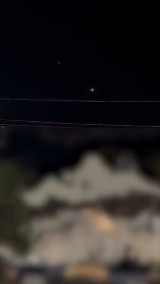 Vertical phone-camera frame at night: a small bright light in a black sky, with the bottom half of the frame blurred by the government to obscure identifying detail