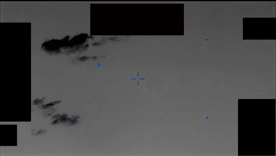 Infrared frame of dark cloud shapes against a pale sky, with black redaction blocks along the top and left edges and a small cyan crosshair near the centre
